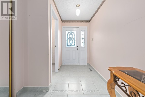 Interior view of a hallway with light pink walls, tiled floor, and glass-paned front door. - 38 Jasper Crescent, Brampton