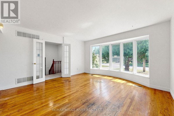 Spacious living area with hardwood floors, a large bay window, and double doors leading to stairs. - 38 Lombardy Crescent, Toronto