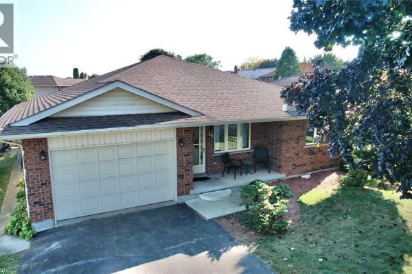Aerial view of a brick bungalow with an attached garage, driveway, and surrounding trees. - 38 Mann Avenue, Simcoe