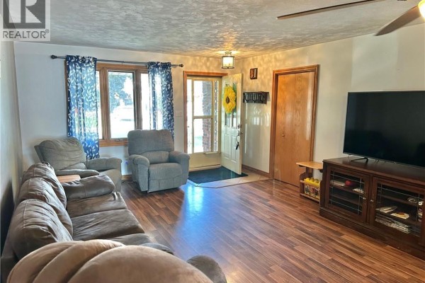 Living room with brown sectional sofa, recliners, wood laminate flooring, and view of the front door. - 38 Mann Avenue, Simcoe