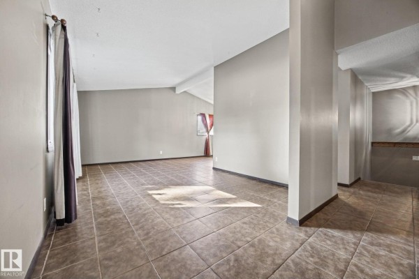 Spacious living area with tan tile flooring, beige walls, and column dividers. - 38 Raven Dr, Sherwood Park