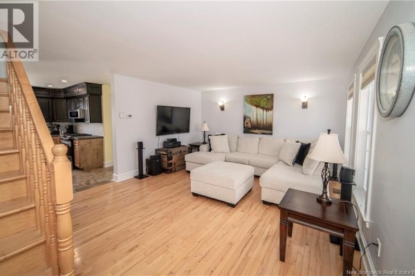 Living room with hardwood floors, a sectional sofa, a television, and an adjoining kitchen. - 38 Red Maple Court, Fredericton