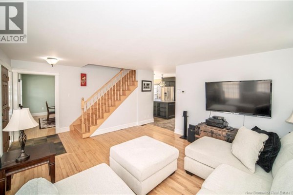 Living room with hardwood floors, a sectional sofa, a television, and a view into the kitchen. - 38 Red Maple Court, Fredericton