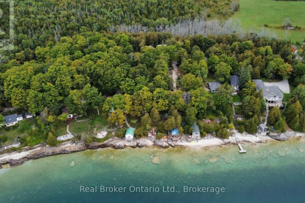 Aerial view of multiple cottages nestled among trees along a rocky shoreline with clear blue water. - 38 Whippoorwill Road, Northern Bruce Peninsula