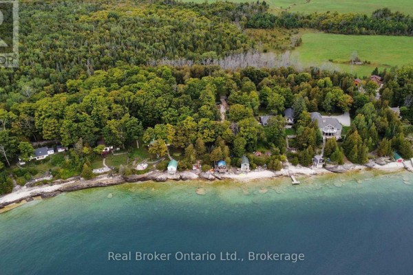 Aerial view of multiple cottages nestled among trees along a rocky shoreline with clear blue water. - 38 Whippoorwill Road, Northern Bruce Peninsula