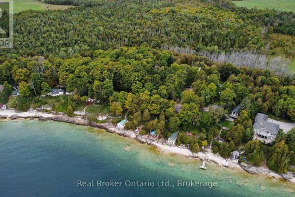 Aerial view of multiple cottages nestled among trees along a rocky shoreline with clear blue water. - 38 Whippoorwill Road, Northern Bruce Peninsula