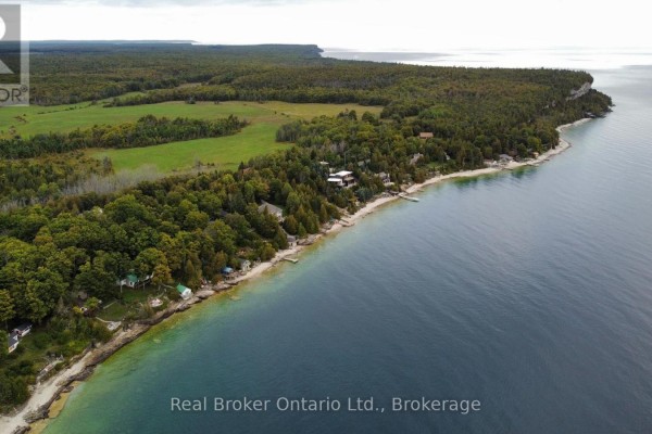 Wide aerial view of a tree-lined coastline with scattered buildings and a vast blue lake under a cloudy sky. - 38 Whippoorwill Road, Northern Bruce Peninsula