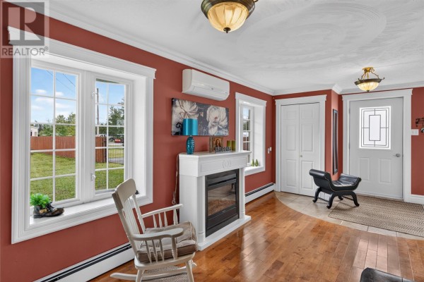 Living room with a white fireplace, rocking chair, and large windows overlooking the yard. - 380-380a Gander Bay Road, Gander