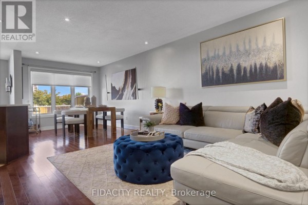 Living and dining area with sectional sofa, blue ottoman, wooden dining table, and artwork. - 380 Goldenbrook Way, Ottawa