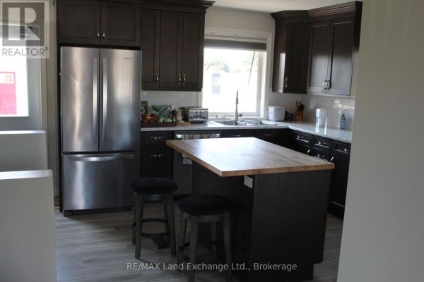 Kitchen with dark brown cabinets, stainless steel refrigerator, and island with seating. - 380 Princes Street S, Kincardine