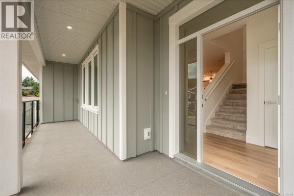 View of a covered balcony with grey flooring and glass railings, opening to interior stairs. - 3800 Marjorie Way, Nanaimo