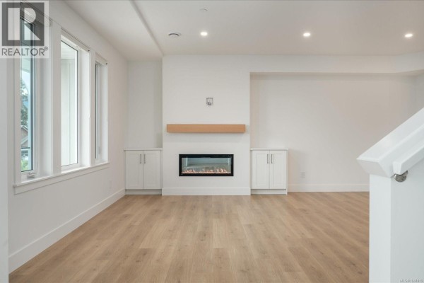 Living room with light wood floors, electric fireplace with built-in cabinets, and large windows. - 3800 Marjorie Way, Nanaimo