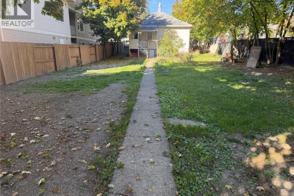 Backyard with a gravel driveway, grass, trees, and a white pickup truck parked near a wooden fence. - 3802 32 Avenue, Vernon
