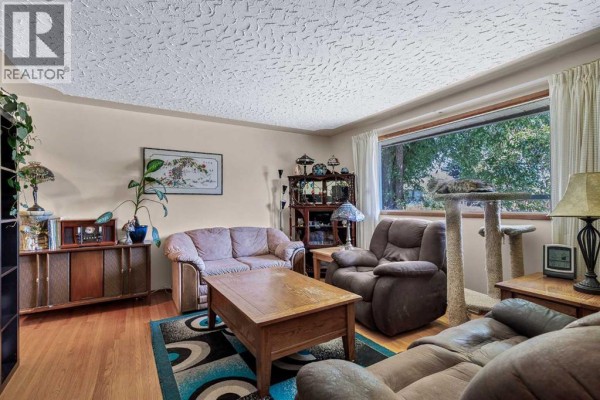 Living room with light beige furniture, wooden floors, a patterned rug, and a large window with curtains. - 3803 4 Avenue Sw, Calgary