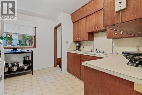 Kitchen with light-colored laminate countertops, wooden cabinets, a double sink, and a window with blinds. - 3803 4 Avenue Sw, Calgary