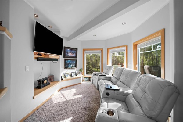 Cozy home theater room with plush reclining white leather chairs and a large flat-screen television. - 38047 38n Road, Ste Anne Rm