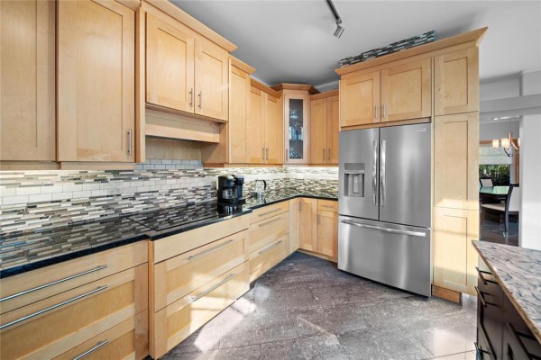 Modern kitchen with light wood cabinetry, granite countertops, stainless steel refrigerator, and tiled backsplash. - 38047 38n Road, Ste Anne Rm