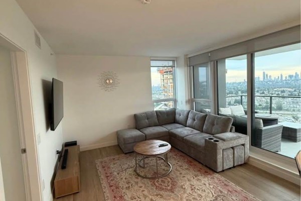 Living room with gray sectional sofa, patterned rug, and city view. - 3805 2135 Springer Avenue, Burnaby