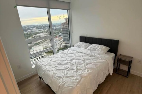 Bedroom with white duvet, nightstand, and large window with city view. - 3805 2135 Springer Avenue, Burnaby