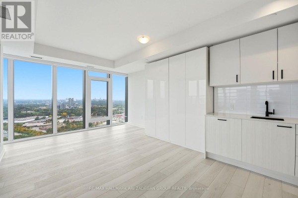 Modern white kitchen with integrated appliances and large windows offering city views. - 3807 - 1 Quarrington Lane, Toronto