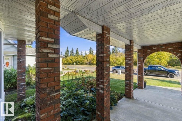 View from the covered porch looking out to the street, showing brick columns and greenery. - 3807 36 Av Nw, Edmonton