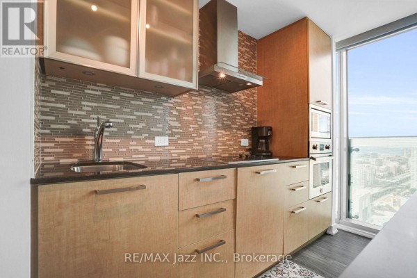 Close-up of kitchen with light wood cabinets, granite countertops, stainless steel backsplash, and sink. - 3808 - 14 York Street, Toronto