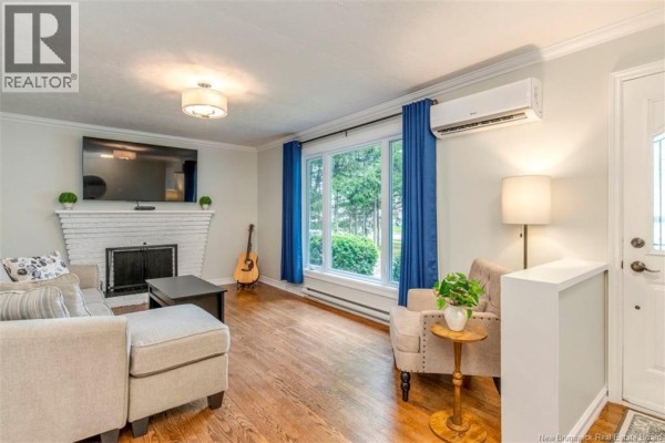 Living room with a white brick fireplace, sectional sofa, and large window with blue curtains. - 381 Beaumont Street, Dieppe