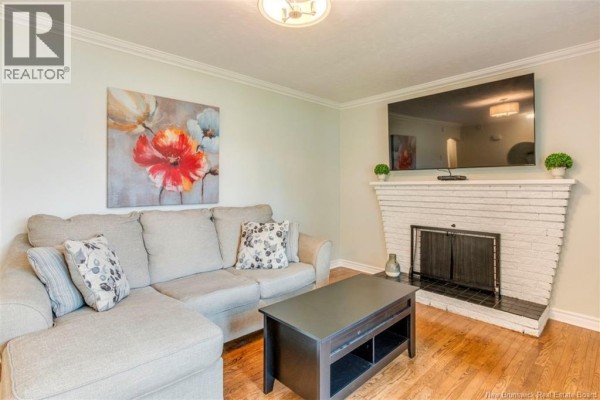 Living room with a sectional sofa, coffee table, and white brick fireplace with a TV above. - 381 Beaumont Street, Dieppe