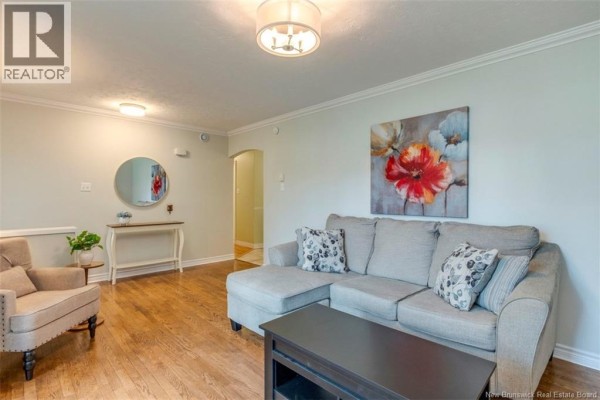 Living room with a sectional sofa, armchair, and a hallway leading to another room. - 381 Beaumont Street, Dieppe