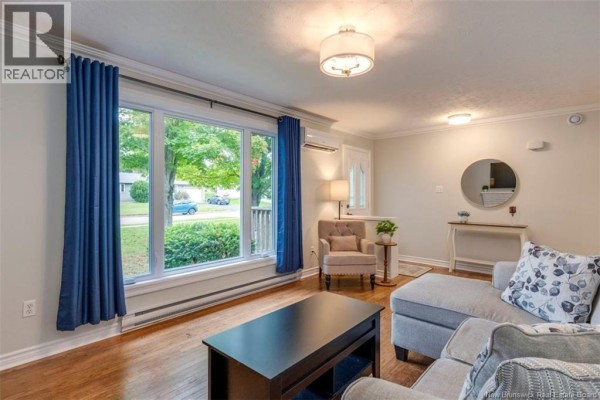 Living room with a sectional sofa, armchair, large window with blue curtains, and entryway. - 381 Beaumont Street, Dieppe