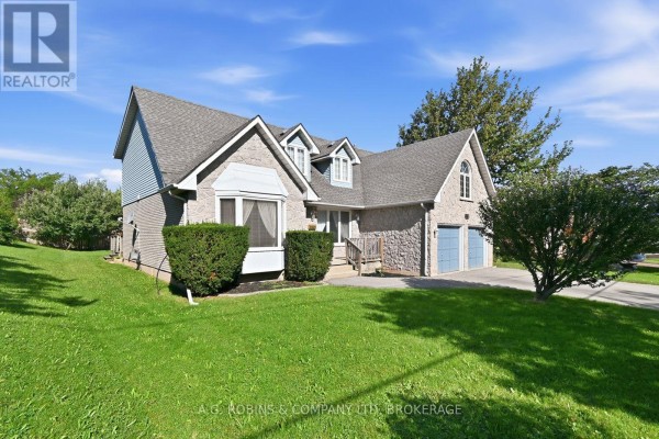 View of the stone house facade featuring a manicured lawn, trees, and a double garage. - 381 Kerman Avenue, Grimsby