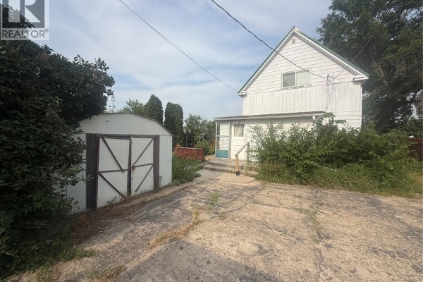 Rear exterior of a white house with a detached metal shed and concrete driveway. - 381 Main Street, Bengough