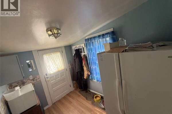 Room with a white door, window with blue curtains, white refrigerator, and beige walls. - 381 Main Street, Bengough