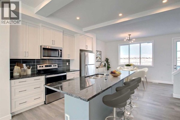 Kitchen with white cabinets, granite countertops, island with bar stools, and stainless steel appliances. - 381 Waterford Boulevard, Chestermere
