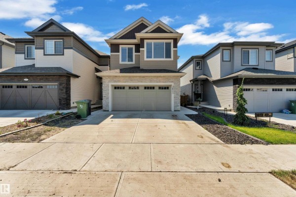 Front exterior of a beige and brown two-story house with a stone accent facade and a double garage. - 3811 42 Av, Beaumont