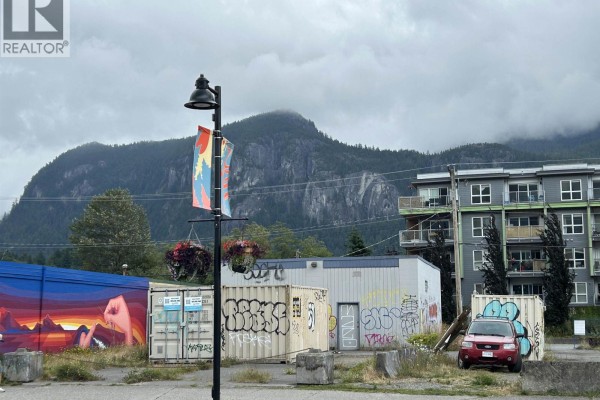 Street view of shipping containers and a building with graffiti, mountains in background. - 38120 Cleveland Avenue, Squamish