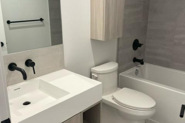 Contemporary bathroom with a white basin sink, black faucet, toilet, and a bathtub with grey tiled walls. - 3815 - 108 Peter Street, Toronto