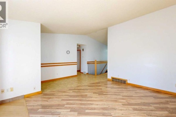 Living room with wood laminate flooring, view of hallway with stairs leading down. - 3818 61a Street, Stettler
