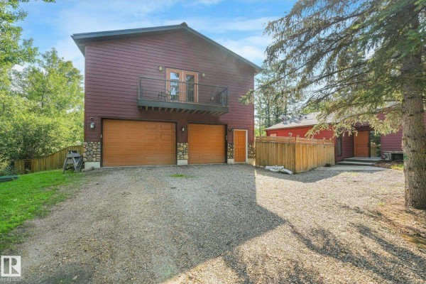 Side view of a red house with a balcony, double garage doors, and wooden fence. - #382 51112 Rge Road 222, Rural Strathcona County