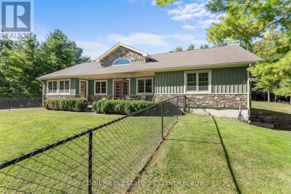 Right side exterior of a green and stone bungalow with a chain-link fence. - 382 Lakehurst Circle Road, Trent Lakes