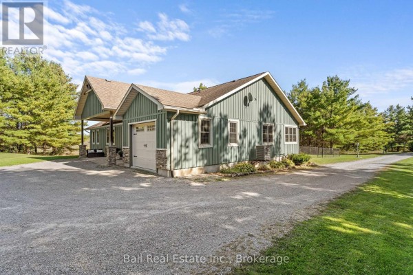 Rear exterior of the green bungalow showing a garage door and gravel driveway. - 382 Lakehurst Circle Road, Trent Lakes