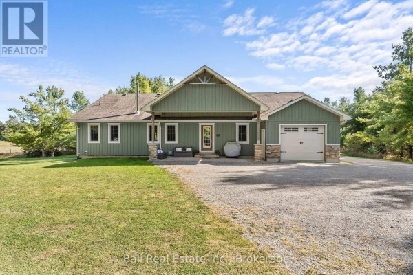 Front and side exterior of the green bungalow with a garage and gravel driveway. - 382 Lakehurst Circle Road, Trent Lakes