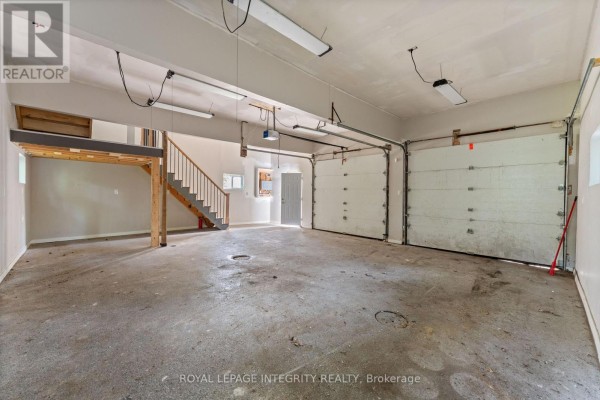 Exterior of a grey detached garage with two white garage doors and a single side door. - 3823 Drouin Road, Clarence Rockland