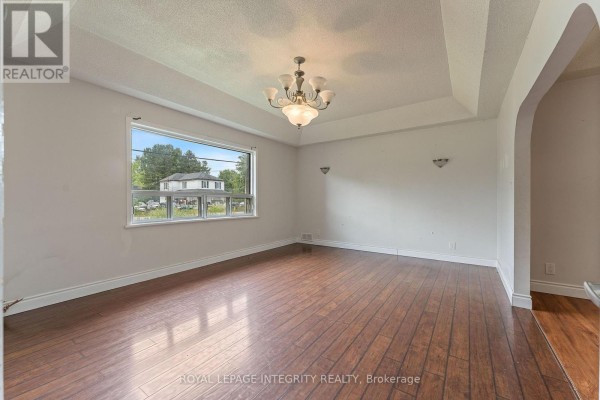 Living room with wood flooring, light grey walls, and doorways leading to other rooms. - 3823 Drouin Road, Clarence Rockland