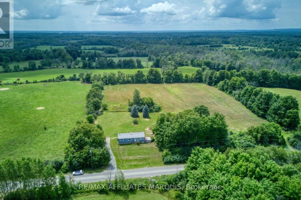 Aerial view of a house surrounded by green fields and trees. - 3826 Big Rideau Lake Road, Rideau Lakes
