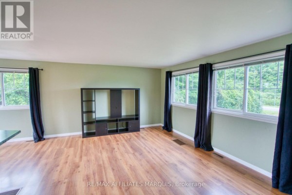 Living room with light green walls, wood laminate flooring, and large windows. - 3826 Big Rideau Lake Road, Rideau Lakes