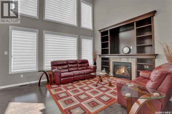 Living room with a fireplace, built-in shelving, a red leather sofa, and a patterned area rug. - 3826 Goldfinch Way, Regina