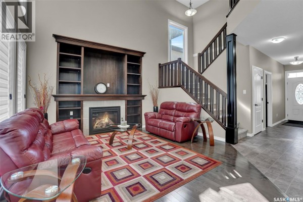Living room showing a fireplace, built-in shelves, red leather sofas, and a staircase leading upstairs. - 3826 Goldfinch Way, Regina