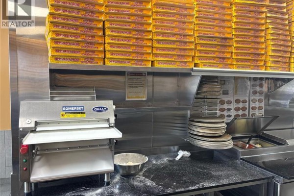 Commercial kitchen counter with a dough roller, pizza pans, and stacks of pizza boxes. - 383 Arthur Street S Unit# 5, Elmira
