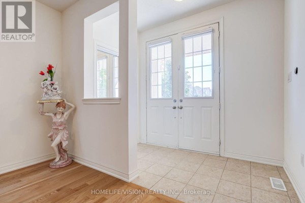 Interior entryway with cream-colored walls, tiled floor, wooden floor, and double glass doors. - 383 Royal West Drive, Brampton